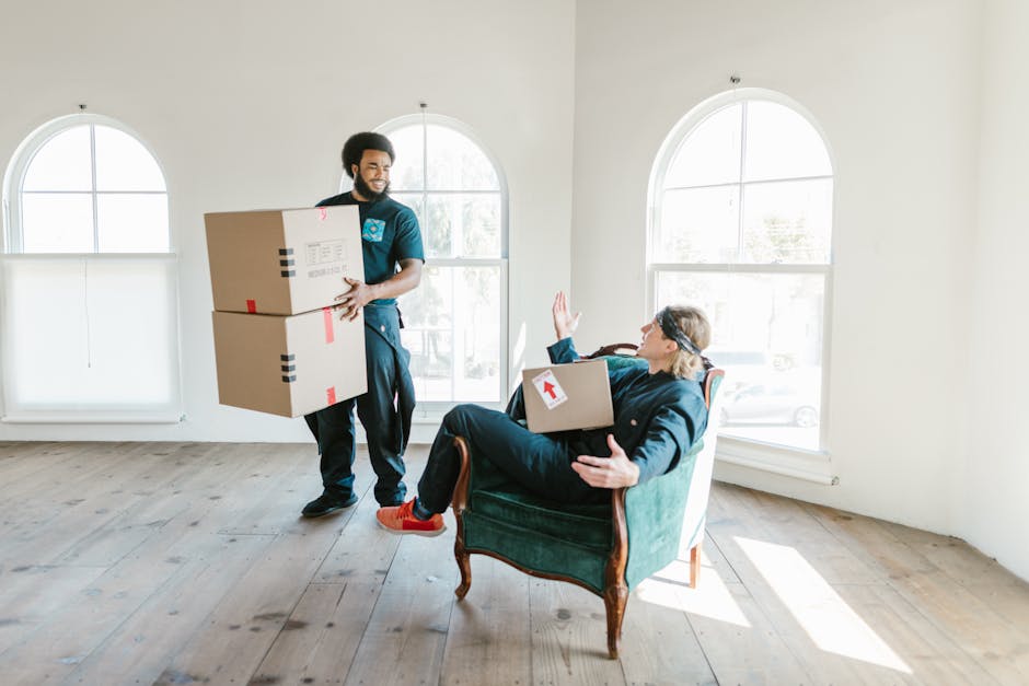 A woman with curly brown hair, dressed in a green T-shirt and blue jeans, is carefully wrapping or unwrapping furniture with protective white plastic or fabric, indicating a home relocation process. S